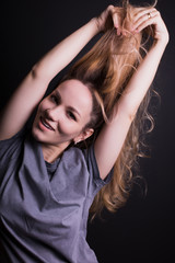 Pretty young model pulling her hair, wears grey shirt,  posing on a black background