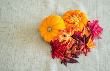 2 small pumpkins covered with colorful autumn leaves on a tan cloth background