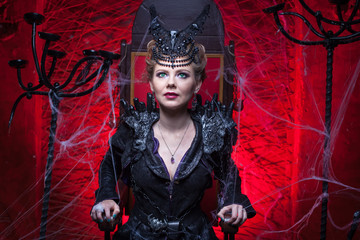 Woman in a sorceress costume sits on a throne in a red room