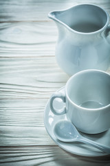 Ceramic cup saucer teaspoon milk jug on wooden board
