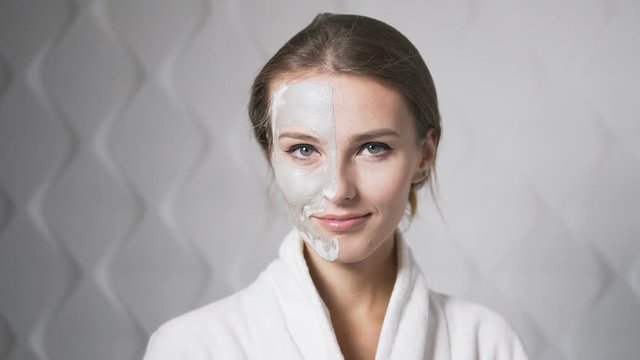 Fair hair woman in white bathrobe showing face mask, indoor shot in the white background