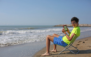 boy with glasses reads an ebook on the beach by the sea in summe