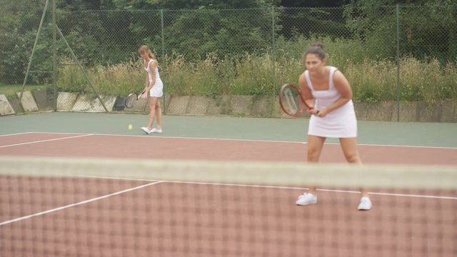  Female doubles tennis players serving & scoring a point on outdoor court