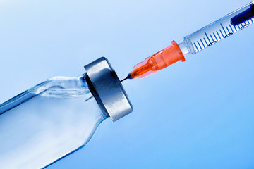 Vial with punctured syringe close up and blue background