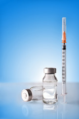 Vials and syringe on white table with blue background vertical