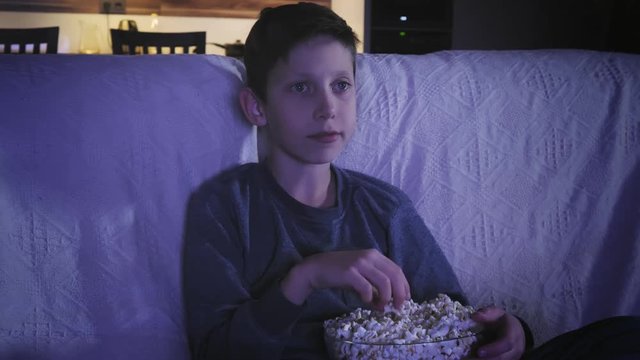 Little boy watching a movie on on TV and eating popcorn