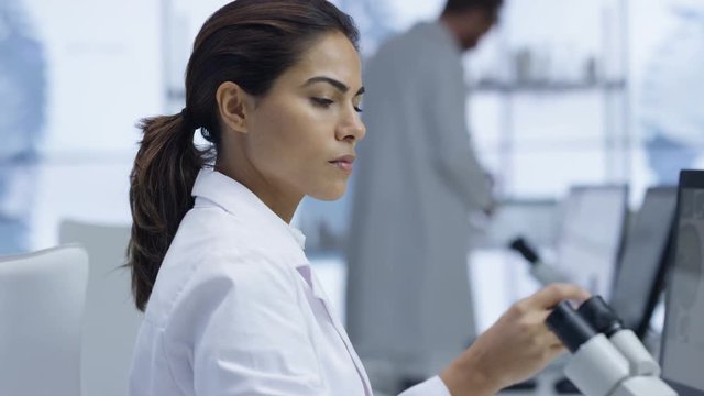  Medical researcher looking at a slide under microscope & working on computer