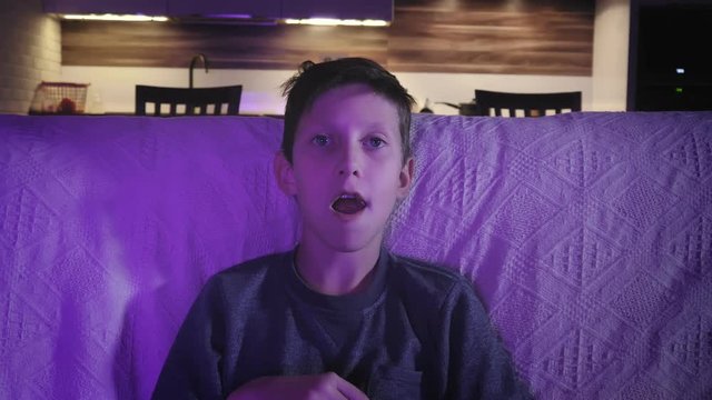 Little boy watching a movie on on TV and eating popcorn