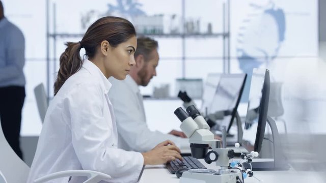 Medical researcher in the lab working on computer & looking into microscope
