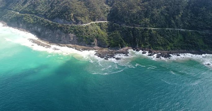 From open sea to Great Ocean road cliff coast with evergreen gumtree covered hills over water break line of waterfront.
