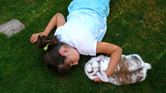 Top view of a little girl petting fluffy white rabbit o green grass, 4k