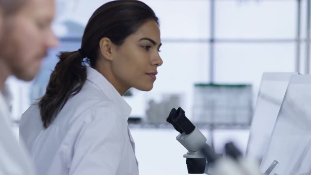  Medical researcher in the lab working on computer & looking into microscope