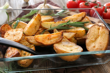 Delicious baked potatoes with rosemary in baking dish on table
