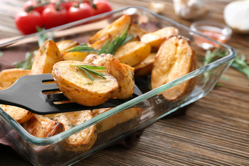 Delicious baked potatoes with rosemary on spatula above baking dish, closeup