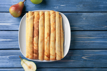 Rolled thin pancakes on white plate against wooden background