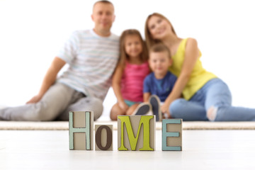 Word HOME made of wooden letters and happy family on background