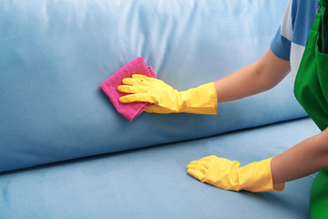 Woman cleaning couch with duster at home