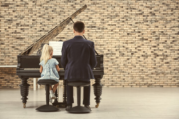 Little girl and young man playing piano indoors