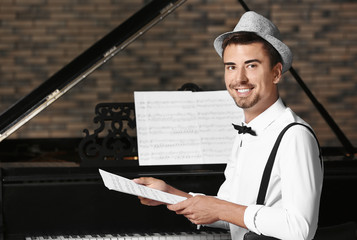 Young man holding music sheets near piano indoors