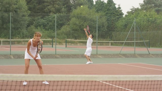  Male & female tennis players serving & scoring a point on outdoor court