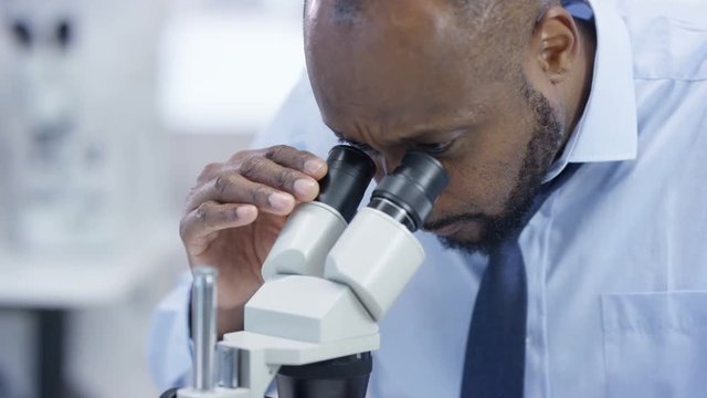  Close up medical researcher in the lab looking at a slide under microscope