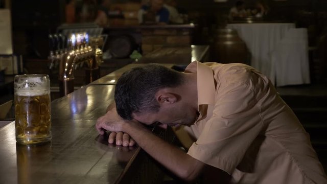 Too drunk guy holding his head on the bar cannot reach his glass