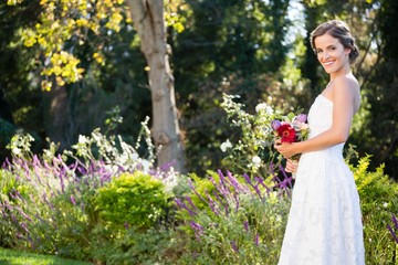 Portrait of smiling bride holding bouquet while standing on