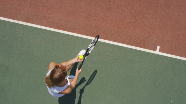  Female tennis player throws ball into the air to serve. Overhead view slowmo - Powered by Adobe