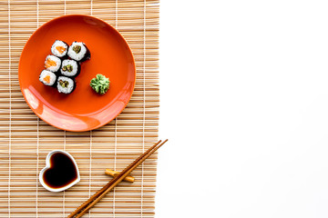 Sushi roll with salmon and avocado on plate with soy sauce, chopstick, wasabi on mat. White background Top view copyspace