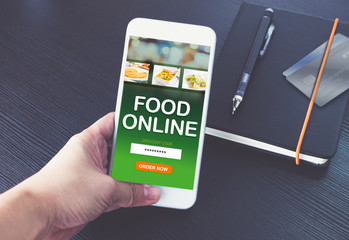 Hand holding mobile phone and order food online for app with promo code with credit card on notebook on black wood table background,Digital marketing concept ,office desk