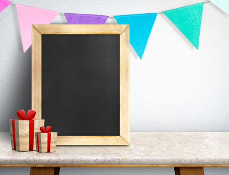 Blackboard with gift box and colorful flag banner on marble table at white wall,Leave space for display or montage of your design, Holiday new year concept.