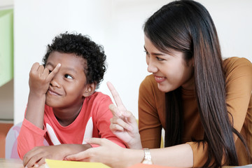 Young asian woman teacher teaching american african kid in kindergarten classroom with happiness and relaxation, kid education concept