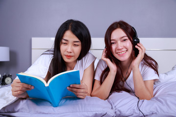 two woman reading a book and using smart phone on bed in bedroom