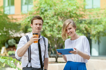 Woman with tablet PC and a man with cup of coffee on a street in sunny summer day
