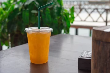Crédence de cuisine en verre imprimé Jus Jus d& 39 orange dans un verre en plastique posé sur une table en bois.