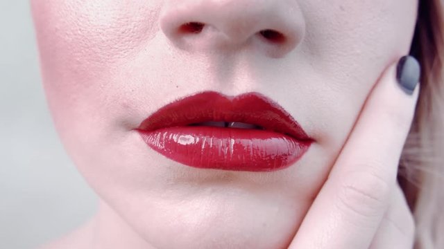 Close-up beautiful chubby lips with bright juicy red lipstick. Face young cute girl. Advertising lipstick. Girl touches her face. She runs finger near her lips. Beauty saloon. Permanent makeup lips.