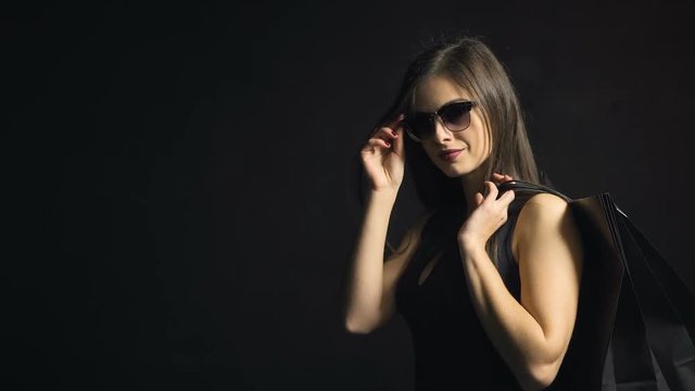 Portrait of beautiful caucasian girl, in cool sunglasses and sexy black dress, on black friday in the black background