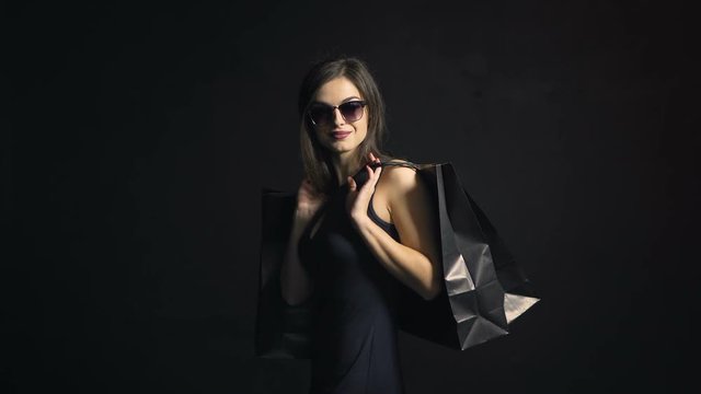 Back view of sexy girl, in elegant black dress, carrying shopping bags on black friday, indoor shot in the black background