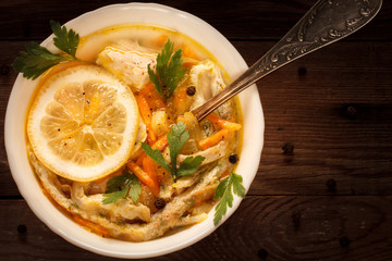 Italian soup with egg noodles, chicken and lemon on a natural wooden background.