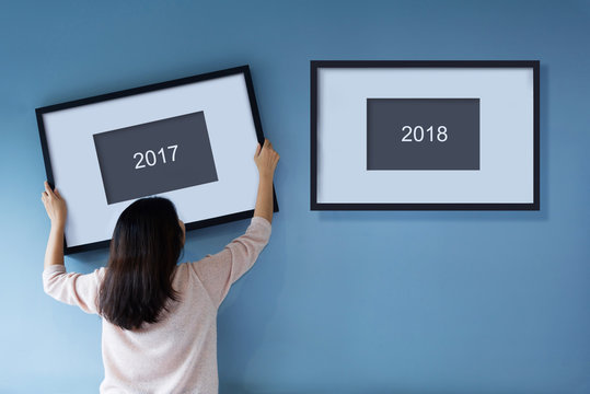 New year concept. Asian woman holding a picture frame of 2018 on blue wall.