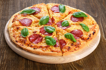 Pepperoni pizza with salami and basil on dark wooden background.