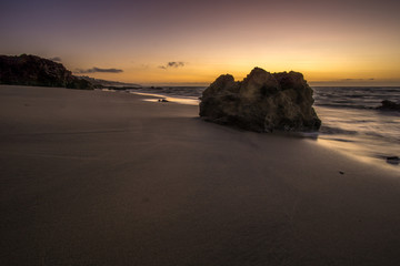 Fototapeta na wymiar a rock on the beach at sunrise and waves