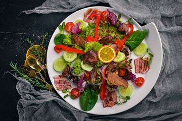 Salad with bacon and chicken liver. On a wooden surface. Top view. Free space for your text.