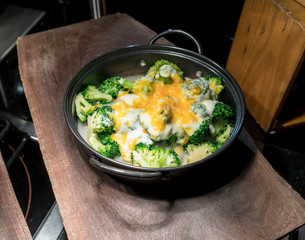 Baked broccoli cheese in black metal sauce pot on wood tray.