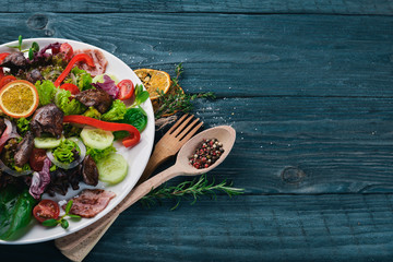 Salad with bacon and chicken liver. On a wooden surface. Top view. Free space for your text.