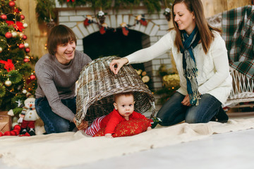 Portrait of young playful happy parents with a cute little baby boy in a decorated room at home. Christmas good mood. New Year. Lifestyle, family and togetherness concept.