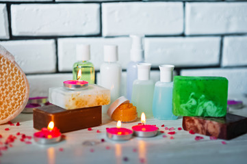 Spa accessories. Small lighted candles, many colored soaps of soap, many different shapes of bottles for the bathroom. The bath salt is pink, the body scrub is showered. Light brick and white wooden a