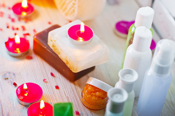 Obraz na płótnie Canvas Spa accessories. Small lighted candles, many colored soaps of soap, many different shapes of bottles for the bathroom. The bath salt is pink, the body scrub is showered. Light brick and white wooden a