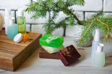 Spa accessories. Sprigs of a Christmas tree, many multi-colored pieces of soap, many different shapes of bottles for a bathroom. Body scrub. Light brick and white wooden as a background