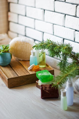 Spa accessories. Sprigs of a Christmas tree, many multi-colored pieces of soap, many different shapes of bottles for a bathroom. Body scrub. Light brick and white wooden as a background